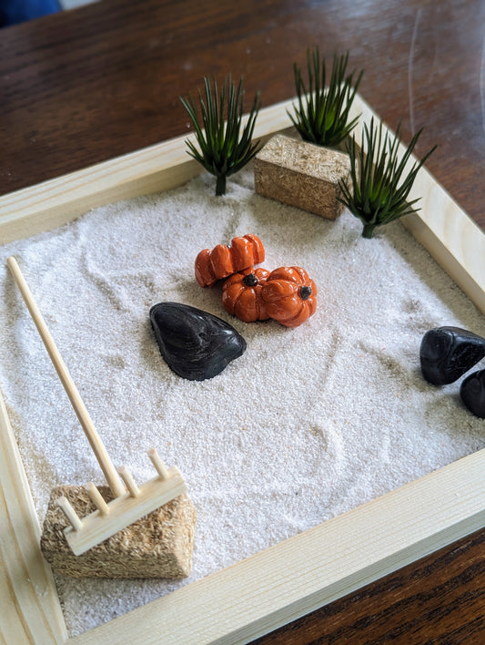 Fall miniature Zen garden with sand, rocks, pumpkins, hay bales, and greenery